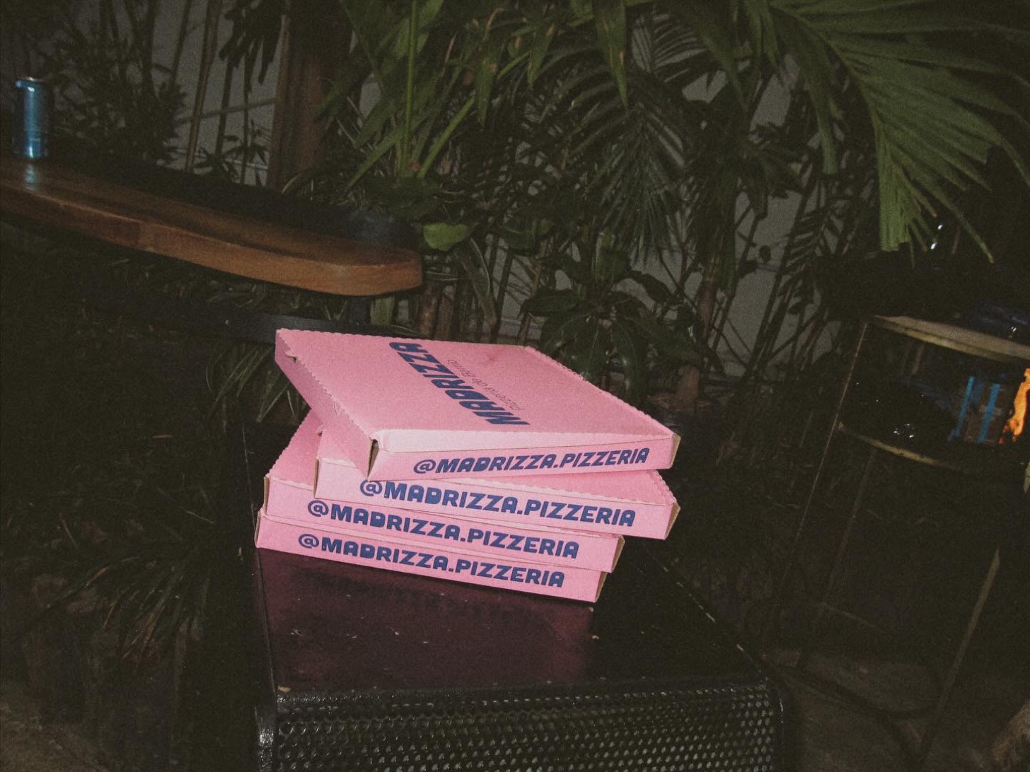 Cajas rosas de Madrizza apiladas de noche, entre palmas